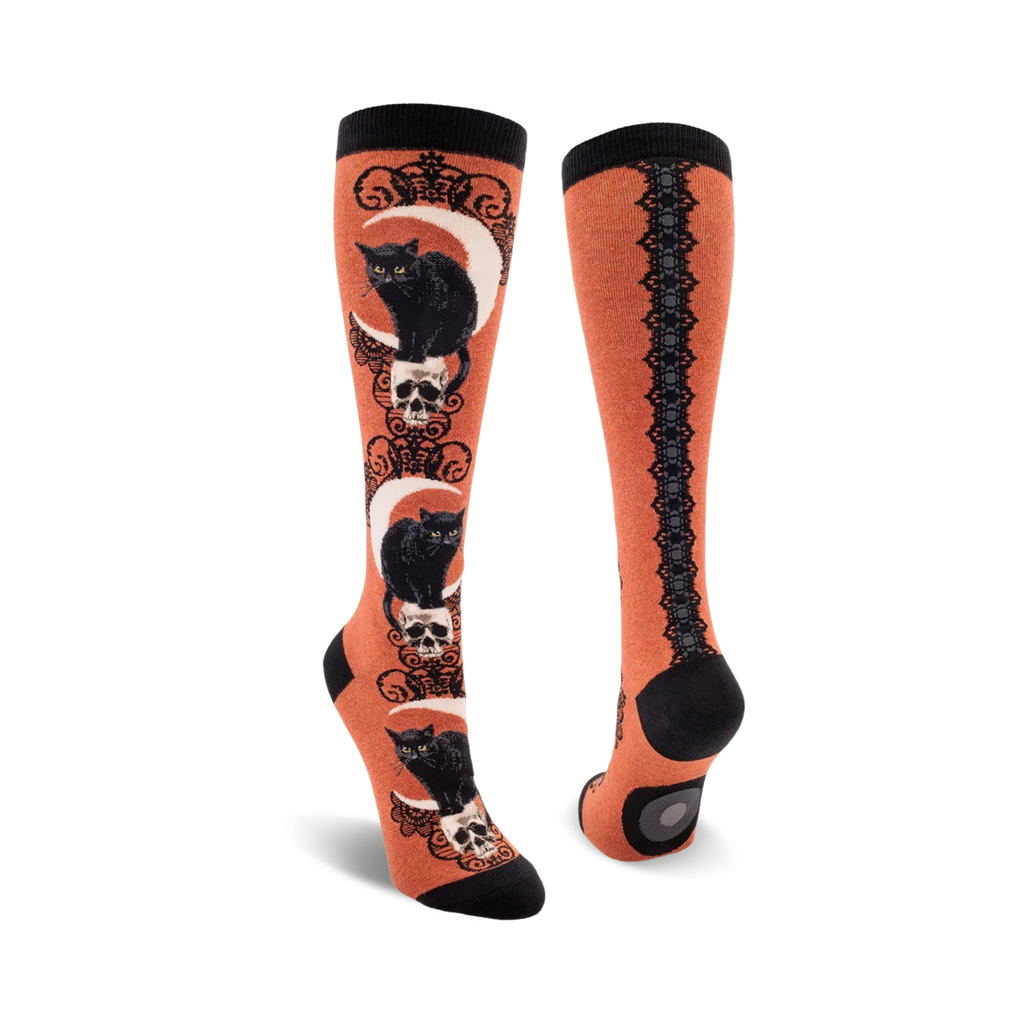 Pair of knee-high socks with black cat and skull design on an orange background