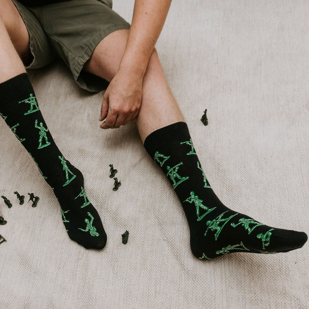 Person wearing black socks with green patterns sitting on a textured surface.