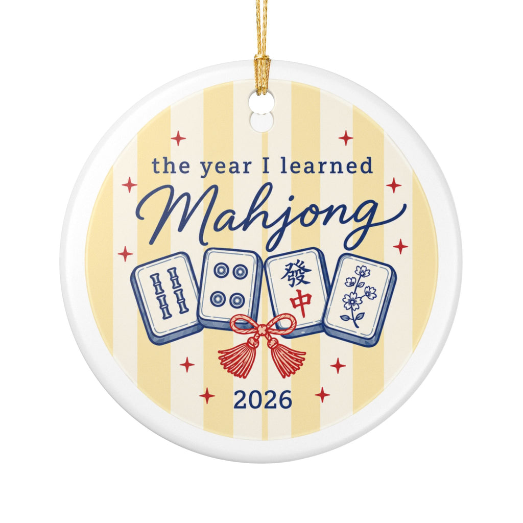 A round ceramic Christmas ornament featuring a mahjong theme. The ornament is white with pale yellow vertical stripes, decorated with four blue and white mahjong tiles, a red tassel, and the text 'the year I learned Mahjong 2026'.