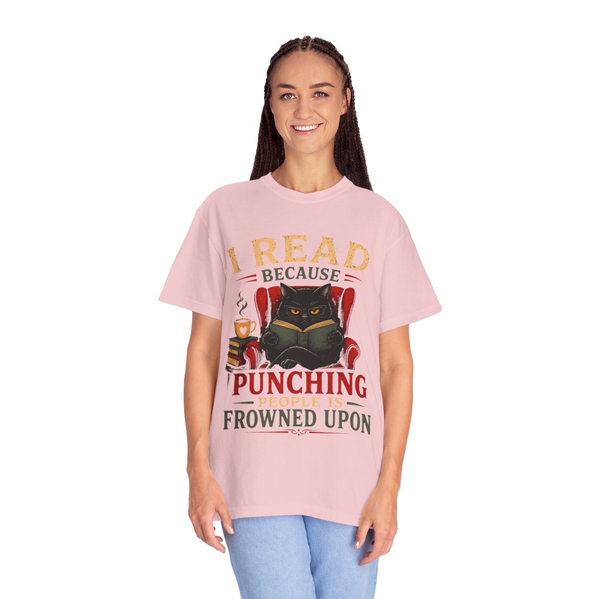 A woman modeling a light pink graphic t-shirt with a design featuring a black cat reading and the text 'I READ BECAUSE PUNCHING PEOPLE ARE FROWNED UPON'. She is wearing light blue jeans against a plain white background.