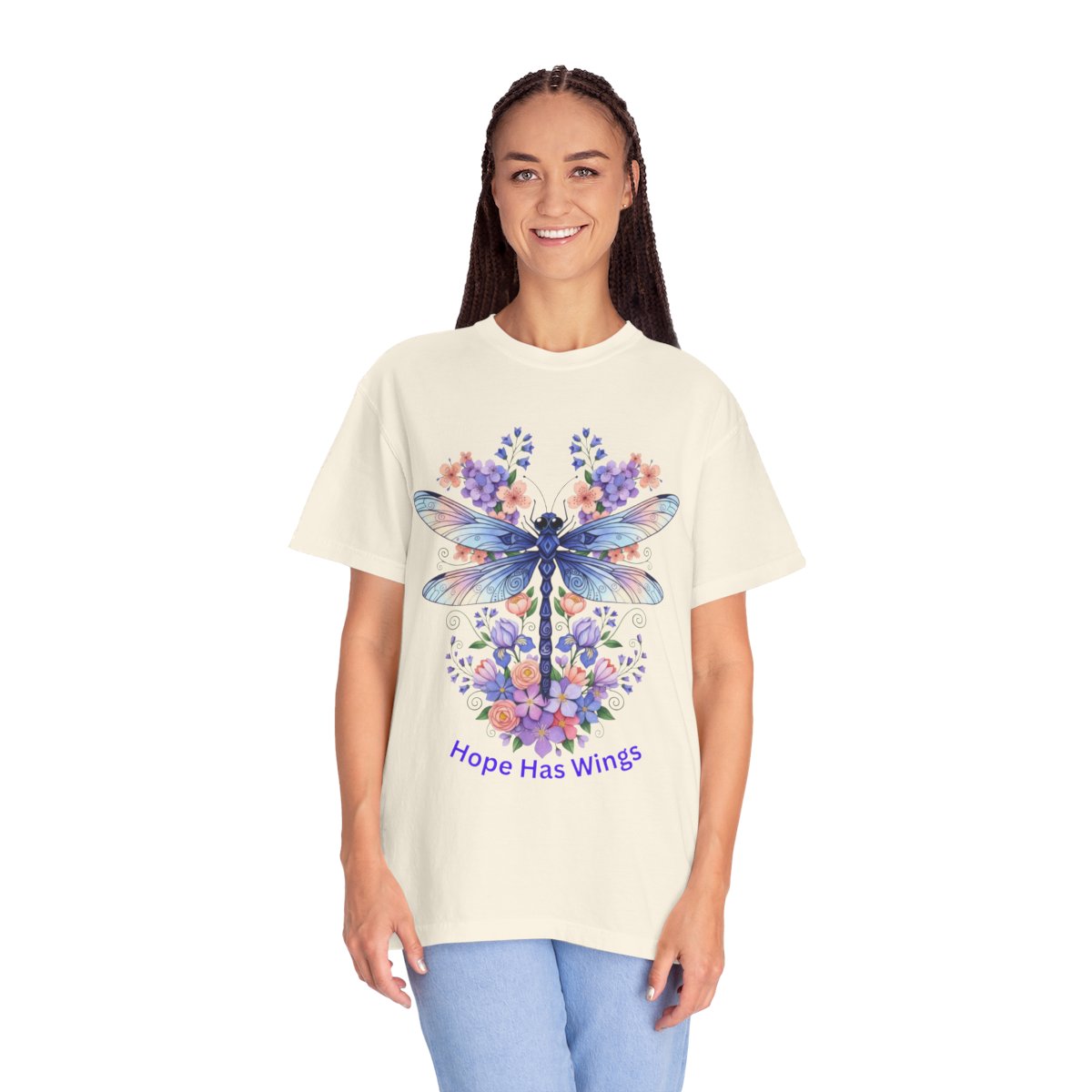 A woman modeling a cream-colored t-shirt with a colorful graphic of a dragonfly surrounded by bluebonnets and the text 'Hope Has Wings' in purple, set against a plain white background.
