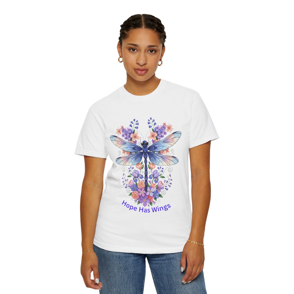 A woman modeling a white short-sleeve crewneck t-shirt with a colorful graphic of a dragonfly surrounded by purple and blue flowers, with the text 'Hope Has Wings' printed below.