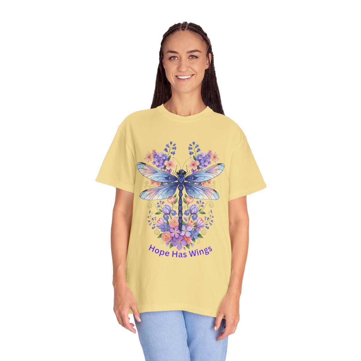 A woman modeling a pale yellow graphic t-shirt featuring a blue dragonfly surrounded by purple and blue flowers, with the text 'Hope Has Wings' printed below. She is wearing light blue jeans against a solid white background.