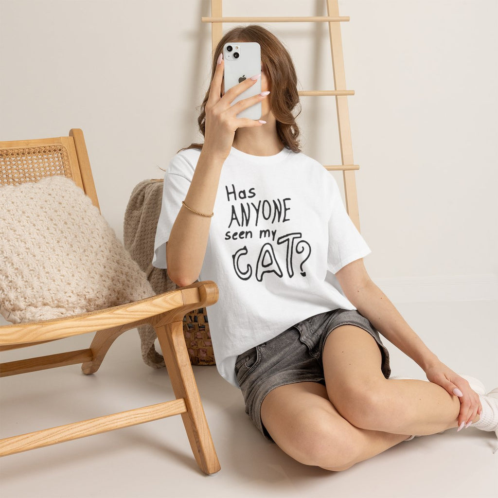 Person wearing a white t-shirt with a black graphic design, sitting on the floor with a wooden chair and ladder in the background.