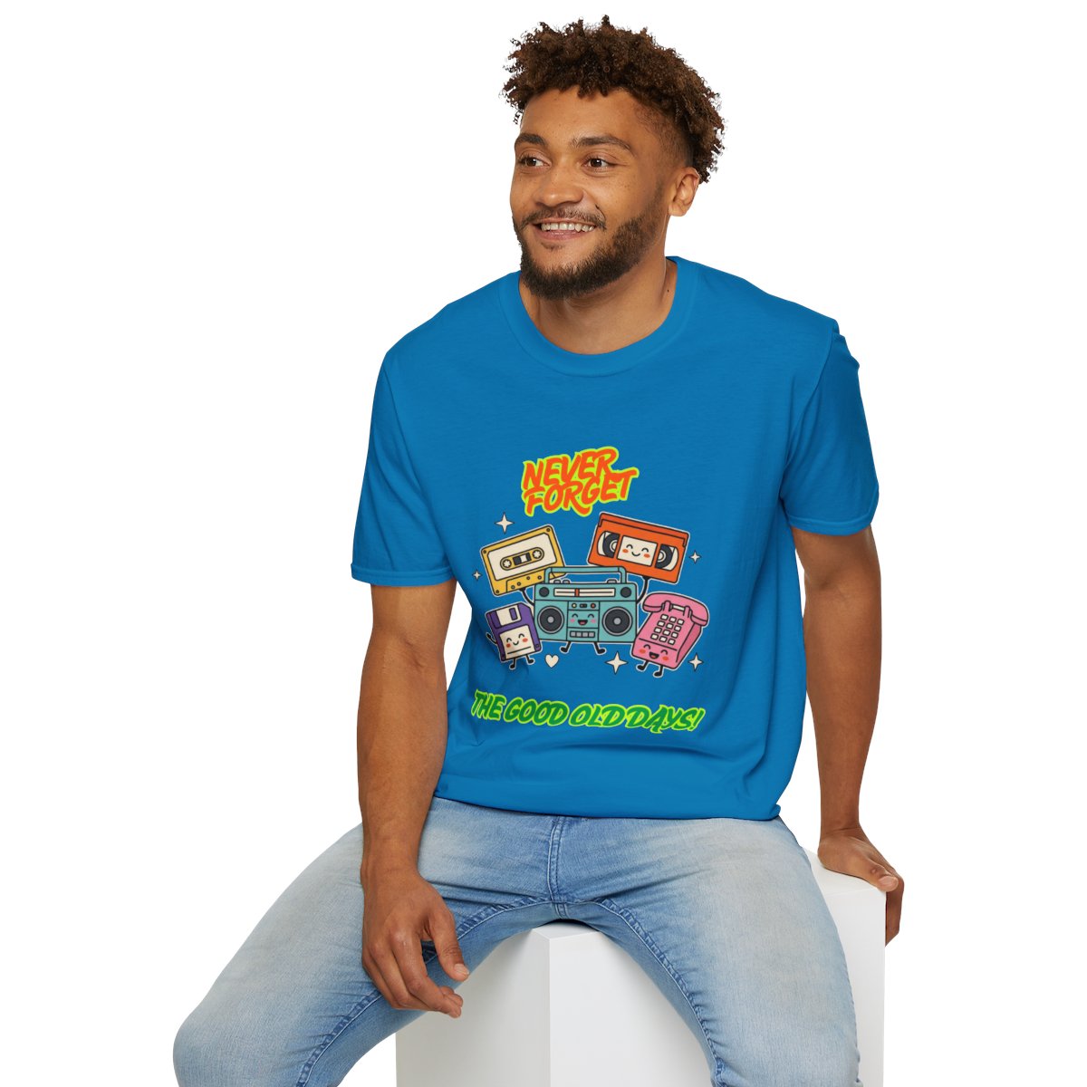 A man wearing a bright blue graphic t-shirt with retro cassette tapes and the text 'HEY! THE GOOD OLD DAYS' sitting on a white block against a white background.