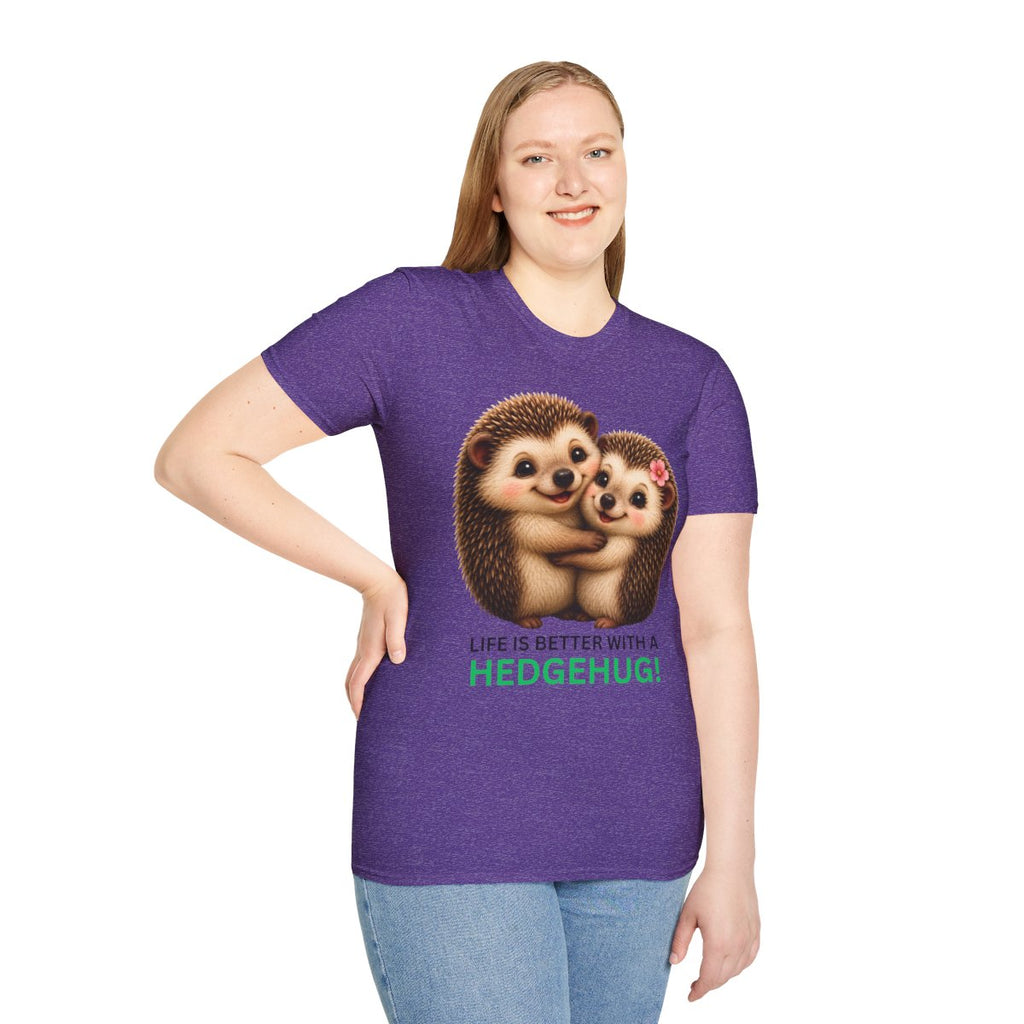 A woman modeling a heather purple short-sleeve t-shirt with a graphic of two hugging hedgehogs and the text 'LIFE IS BETTER WITH A HEDGEHUG!' in green and pink, paired with light blue jeans against a plain white background.
