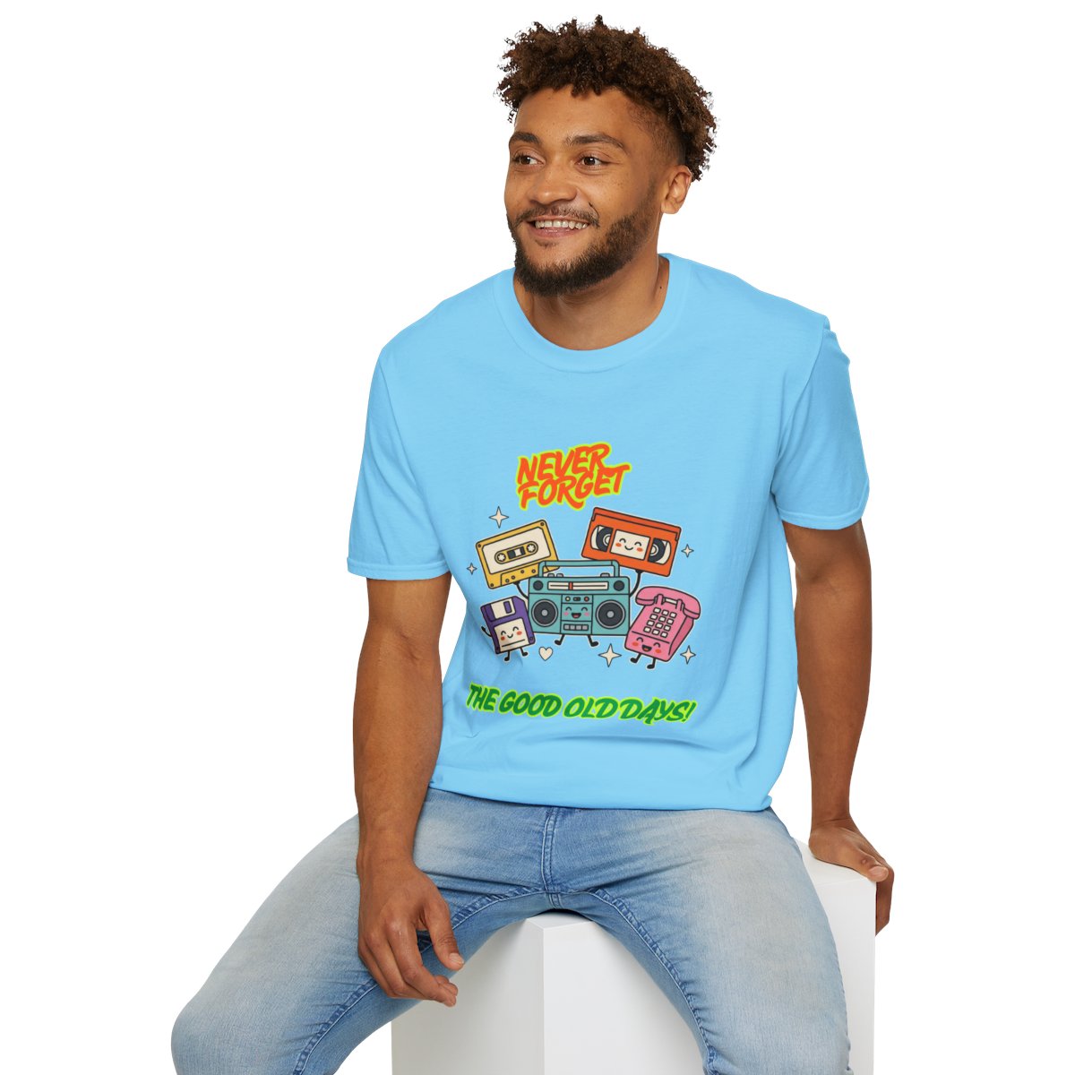 A man wearing a light blue graphic t-shirt with retro cassette tapes and the text 'Never Forget The Good Old Days!' sitting on a white block against a white background.