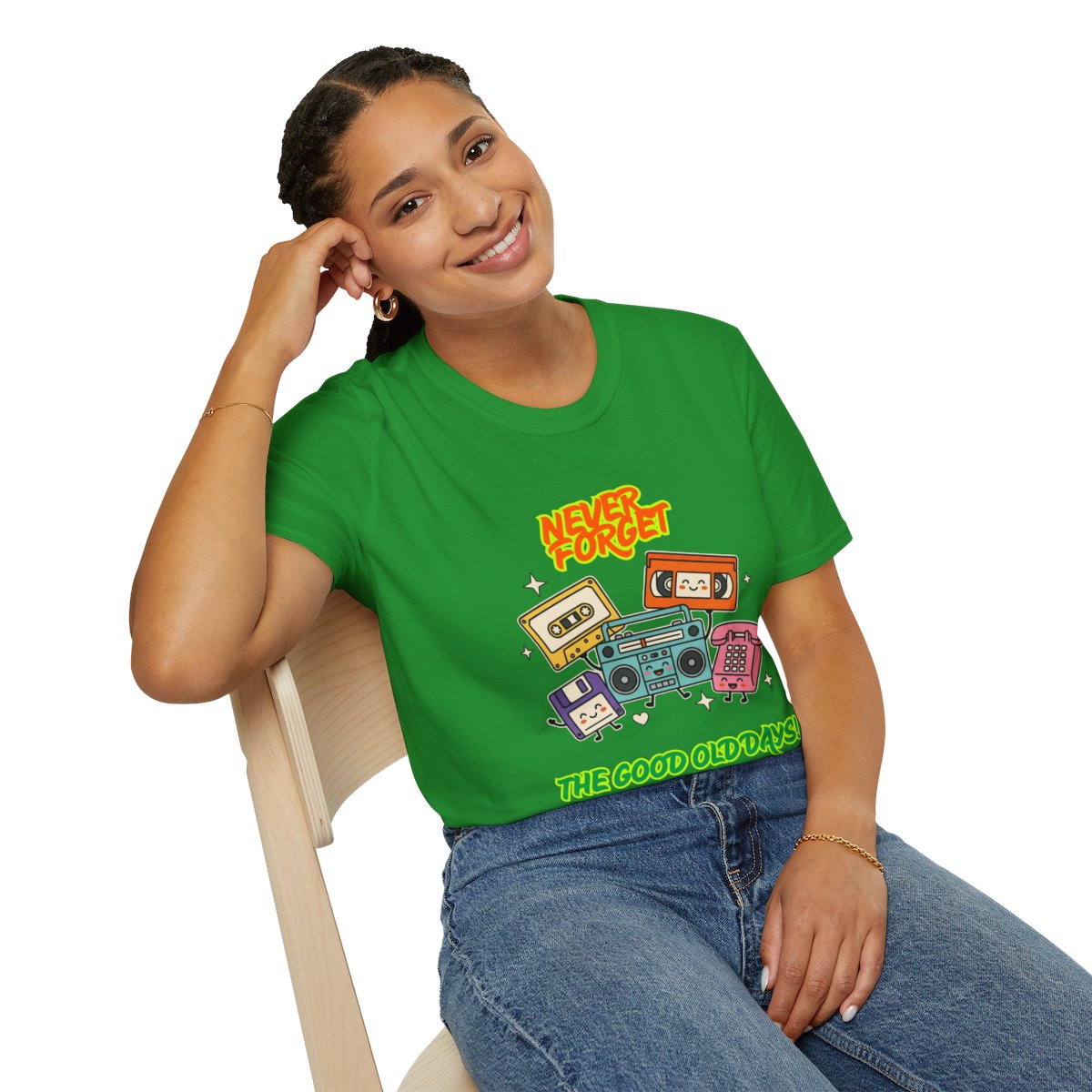 A woman sitting on a light wood chair wearing a bright green graphic t-shirt with retro cassette tapes and boomboxes, paired with blue jeans, against a solid white background.