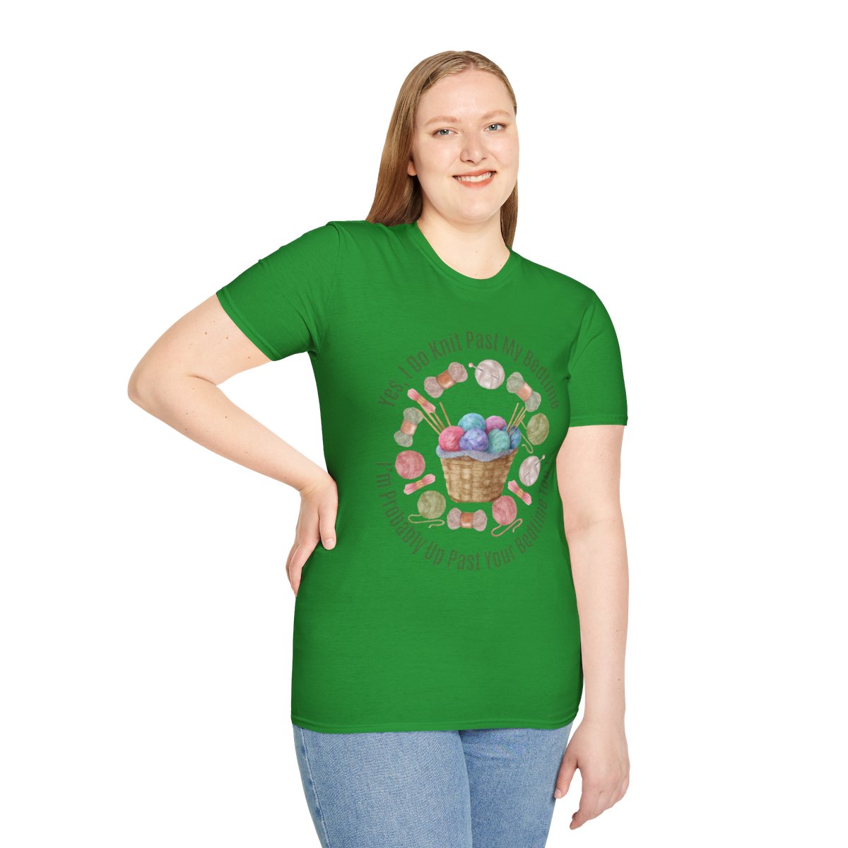 A woman modeling a bright green short-sleeve t-shirt with a colorful knitting-themed graphic on the front, paired with light blue jeans, against a plain white background.